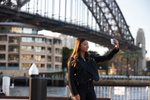 Young woman with mobile phone in front of harbour bridge - Australian Stock Image