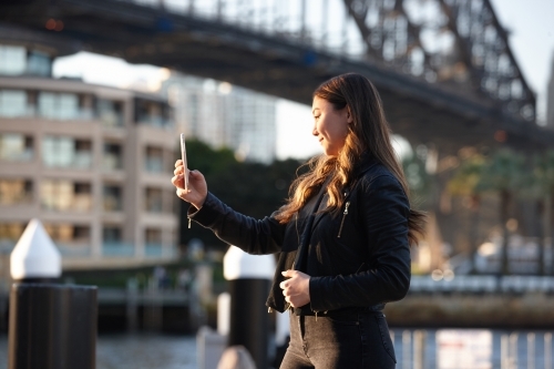 Young woman with mobile phone in front of harbour bridge - Australian Stock Image