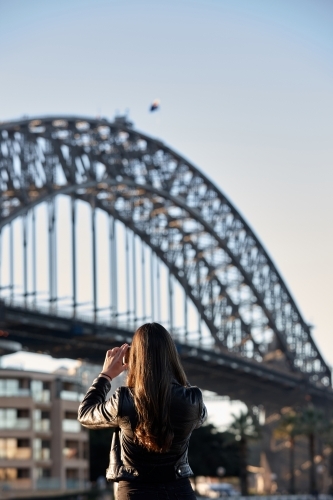 Young woman with mobile phone in front of harbour bridge
