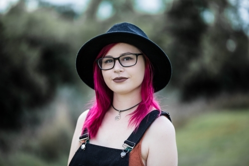 Young woman with pink hair glasses and hat looking serious - Australian Stock Image