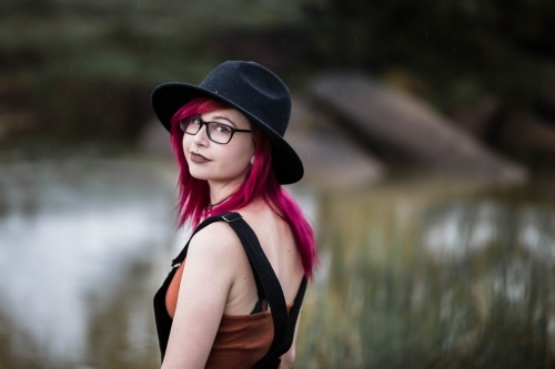 Young woman with pink hair hat and glasses looking over shoulder