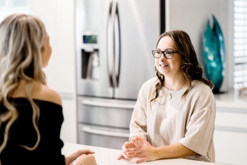 young women talking in kitchen, one sister has Down Syndrome - Australian Stock Image